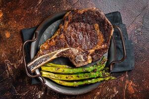 BBQ Grilled Tomahawk or Cowboy with bone beef steak, roasted asparagus. Wooden background. Top view photo