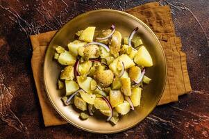 Warm Potato salad with red onion, capers, greens in a plate. Dark background. Top view photo