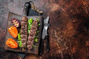 Turkish adana kebab, ground beef and lamb meat grilled on skewers served with tomato, salad and onion. Dark background. Top view. Copy space photo