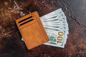 One hundred dollar bill in a brown leather wallet with credit cards. Brown background. Top view. Copy space photo