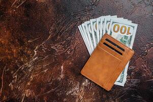 One hundred dollar bill in a brown leather wallet with credit cards. Brown background. Top view. Copy space photo