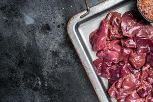 Raw chicken liver meat in steel tray with spices. Black background. Top view. Copy space photo