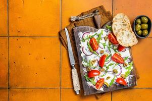Trendy Butter Board with olives, onion, arugula, capers and tomato, Butterboard. Orange background. Top view. Copy space photo