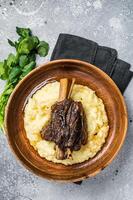 Braised lamb shank on the mashed potato in a plate. Gray background. Top view photo