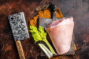 Fresh Raw pork shank knuckle on a butcher board with herbs for cooking. Dark background. Top view photo