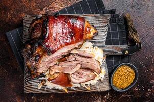 Schweinshaxe Roasted Pork Ham Hock, knuckle with Sauerkraut served on a wooden board. Dark background. Top view photo