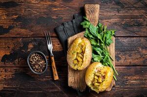 Kumpir, baked Jacket potatoes stuffed with cheese, bacon, salty cucumber, herbs and butter. Wooden background. Top view photo