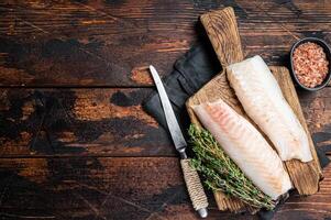 Cod fish fillets, raw codfish with thyme on wooden board. Wooden background. Top view. Copy space photo