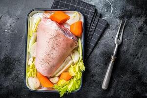 Cooking of Schweinshaxe from Raw pork shank knuckle with vegetables and herbs. Black background. Top view photo