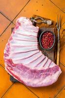 Raw rack of lamb mutton ribs on butcher board with spices. Orange background. Top view photo