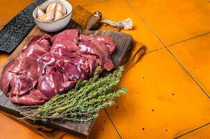 Raw chicken liver, fresh fowl giblets on wooden board. Orange background. Top view. Copy space photo