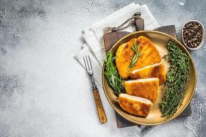 Chicken fried Cordon bleu cutlet with ham and cheese on a plate with herbs. White background. Top view. Copy space photo