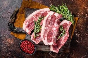 Raw fresh saddle of lamb mutton with herbs and spices on butcher board. Dark background. Top view photo