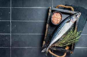 Raw mackerel fish with herbs and spices in wooden tray ready for cooking. Black background. Top view. Copy space photo