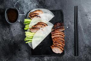 Traditional served Peking Duck with cucumber, green onion, in wheaten chinese pancakes. Black background. Top view photo