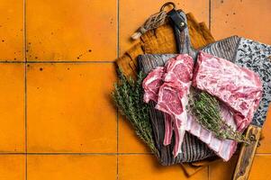 Raw lamb meat chops cutlets on butcher cutting board. Orange background. Top view. Copy space photo