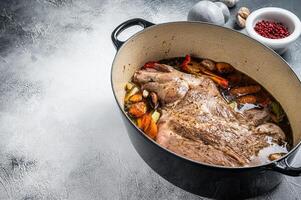 Braised lamb mutton shoulder in a baking dish with vegetables in red wine. White background. Top view. Copy space photo