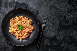 Turkish Menemen, Eggs with tomatoes, green peppers and green onion. Black background. Top view. Copy space photo