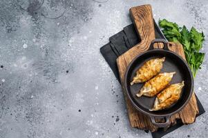 Fried Korean Dumplings with meat and vegetables in skillet. grey background. top view photo