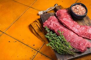 Butcher table with Raw lamb tenderloin Fillet, Mutton loin Meat with thyme. Orange background. Top view. Copy space photo
