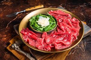 Carpaccio Beef meat appetizer with parmesan and arugula. Dark background. Top view photo