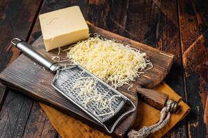 Piece of semi hard cheese and grated cheese with grater. Wooden background. Top view photo