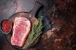 Uncooked Raw striploin or club steak on wooden board with thyme. Dark background. Top view. Copy space photo