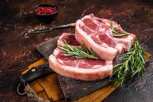 Raw fresh saddle of lamb mutton with herbs and spices on butcher board. Dark background. Top view photo