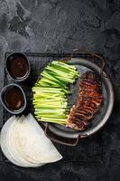 Peking Duck served with cucumber, green onions, and roasted wheaten chinese pancakes with sauce Hoysin. Black background. Top view photo