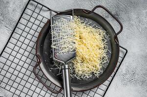 Grated cheese for cooking in a steel tray with grater. White background. Top view photo