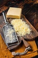 Piece of semi hard cheese and grated cheese with grater. Wooden background. Top view photo