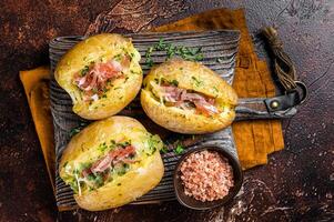 Jacket potatoes baked with cheese, herbs and butter. Dark background. Top view photo