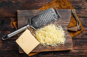 Piece of semi hard cheese and grated cheese with grater. Wooden background. Top view photo