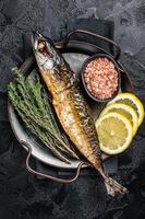 Baked Mackerel Scomber fish in steel tray with thyme and lemon. Black background. Top view photo
