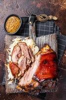 Schweinshaxe Roasted Pork Ham Hock, knuckle with Sauerkraut served on a wooden board. Dark background. Top view photo