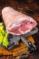 Fresh Raw pork shank knuckle on a butcher board with herbs for cooking. Dark background. Top view photo