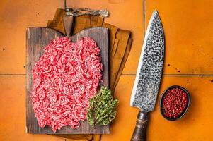 Fresh Raw Mince, Ground beef and pork meat on a butcher board. Orange background. Top view photo
