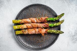 Plate with pork bacon wrapped asparagus on grey table. White background. Top view photo