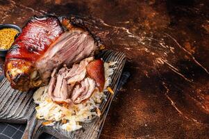 Schweinshaxe Roasted Pork Ham Hock, knuckle with Sauerkraut served on a wooden board. Dark background. Top view. Copy space photo