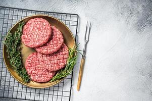Raw minced beef burgers with spices on steel plate with rosemary and thyme. White background. Top view. Copy space photo