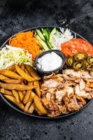 Shawarma Doner kebab on a plate with french fries and salad. Black background. Top view photo