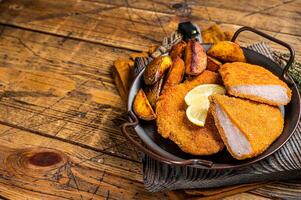 Delicious crispy pork schnitzel with fried potato wedges. Wooden background. Top view. Copy space photo
