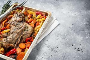 Roast lamb mutton shoulder meat in a baking dish with vegetables. Gray background. Top view. Copy space photo