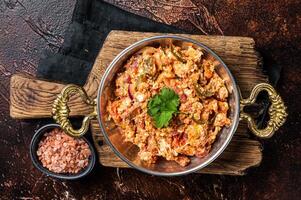 Turkish Menemen omelet with vegetabls and sucuk in askillet. Dark background. Top view photo