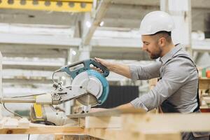 Carpenter cutting wooden plank using circular saw in workshop photo