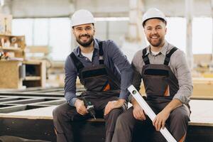 Construction workers smiling and holding tools in modular building factory photo