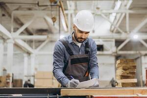 Supervisor writing on clipboard, inspecting wood in modular building factory photo