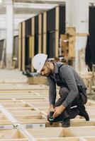 Carpenter using cordless drill assembling modular house in factory photo