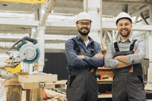 Two smiling carpenters posing with arms crossed in their workshop photo