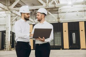 Engineers discussing a project using laptop in modular building factory photo